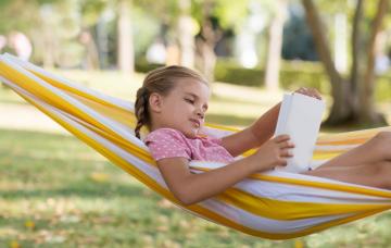 Aprender durante las vacaciones sin ir a la escuela Nia rubia tumbada en verano en una hamaca leyendo un libro
