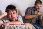 La salud metal de los niños se puede deteriorar si sus padres abusan del smartphone Niño con gesto de aburrimiento mientras su padre usa su smartphone