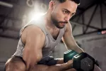 Hombre levanta pesas para ganar músculo Hombre joven musculado entrena con mancuernas en un gimnasio