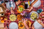 Dieta mediterránea disfruta entre amigos y familia Mesa con mantel de cuadros y varias personas cogiendo comida de platos diversos de la dieta mediterránea