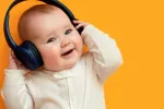 Un bebé de pocos meses sonríe sujetando unos auriculares en sus oídos Bebé muy sonriente con unos auriculares