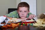 Niño sentado a la mesa rodeado de alimentos inadecuados