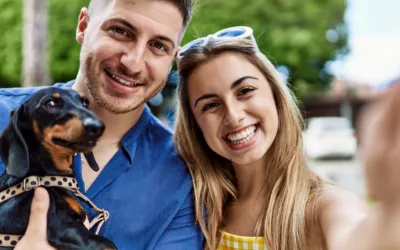 Perro pequeño en brazos de su dueño mira a la cámara del móvil Una joven pareja con su perro en brazos se hace un selfie