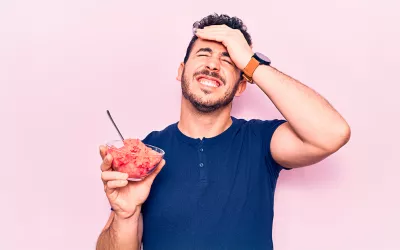 Brain freeze: dolor de cabeza por alimentos fríos Hombre joven con sensación de dolor de cabeza tras comer helado