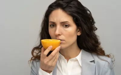 Pérdida de olfato y su relación con el párkinson Mujer morena no es capaz de oler una naranja que sostiene con su mano