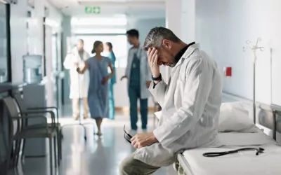 Profesional sanitario con gesto de abatimiento durante su jornada laboral Médico sentado sobre una camilla se toca la frente con gesto abatido