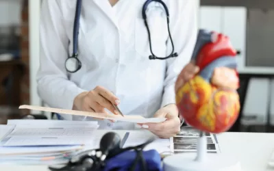 Cardiólogo examina un cardiograma junto a un modelo de corazón Cardiólogo examina un cardiograma con un modelo de corazón artificial en primer plano