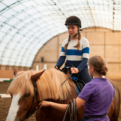 Chica aprendiendo a montar a caballo