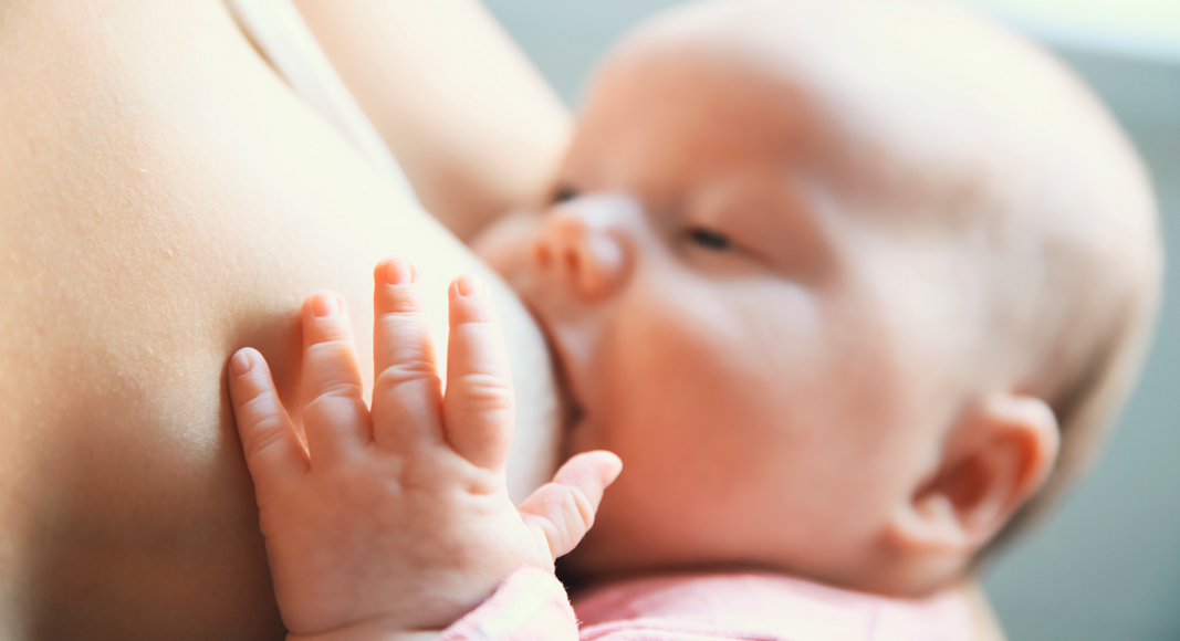 Bebé mamando del pecho de su madre en verano