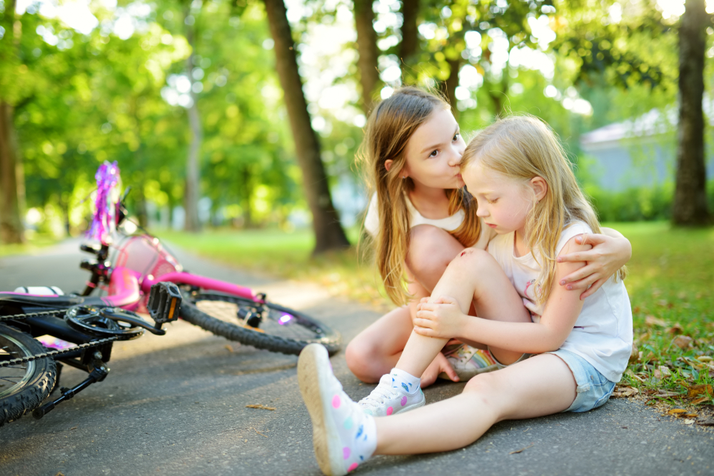 Niña consolando a su amiga porque se ha caído de la bicicleta