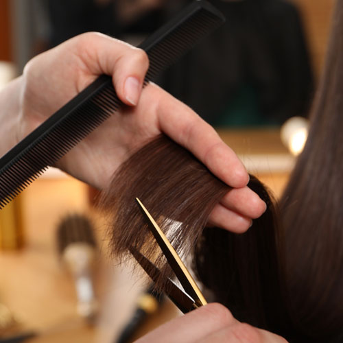 Mujer cortándose las puntas de su pelo en la peluquería