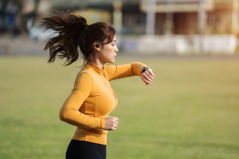 Contar pasos mientras practica la caminata japonesa Chica corriendo en el parque mira su pulsera inteligente