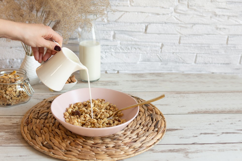 Cuenco de granola con leche Mujer sirviendo leche vegetal sobre un cuenco rosa de granola