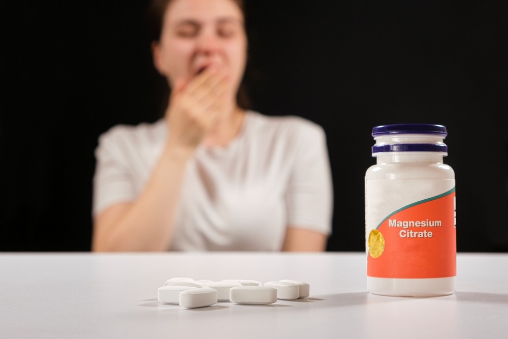Suplementos de magnesio para dormir mejor Mujer bosteza desenfocada con un bote de suplementos de magnesio sobre la mesa