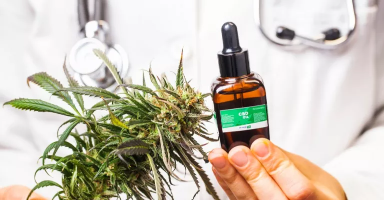 Doctor sostiene unas hojas de marihuana y un bote de CBD