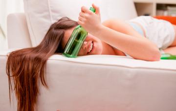 Fases y signos de una intoxicación etílica Una joven tumbada en un sofá sujeta una botella