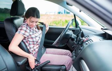 Mujer sentada en el coche colocándose el cinturón de seguridad para evitar lesiones y accidentes.