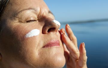 Prevención del cáncer de piel Una mujer se aplica crema bronceadora en la cara