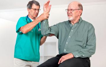 Síntomas de la enfermedad de Paget Un médico examina el brazo a un hombre mayor