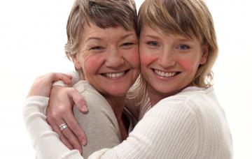 Madre e hija, ambas con rosácea, se abrazan sonriendo a la cámara