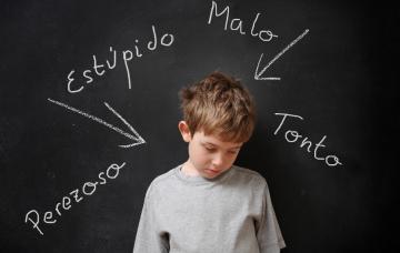 Niño con hiperactividad o TDAH delante de una pizarra con descalificativos