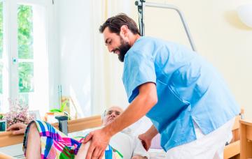 Cómo movilizar a una persona mayor encamada Un cuidador atiende a una persona mayor encamada