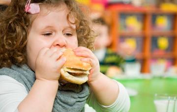 Niña con obesidad infantil comiendo una hamburguesa
