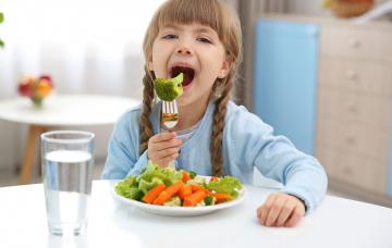 Niña vegetariana comiendo brócoli