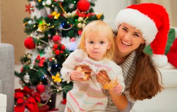 Madre sosteniendo a su bebe comiendo junto al árbol de navidad