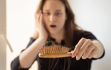Alopecia posparto: causas, soluciones y cuándo preocuparse Mujer mirando asombrada el cepillo del pelo lleno de cabello