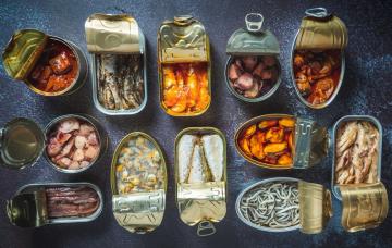 Latas de conservas de pescados abiertas, ¿saludables? Diversas latas de conservas de pescados abiertas sobre una tabla de pizarra