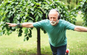 Prueba de equilibrio a una prueba para comprobar cómo envejeces Hombre de edad avanza hace equilibrio sobre una sola pierna en un jardín escuchando música