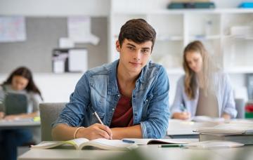 Estudiante con buen rendimiento académico Estudiante moreno adolescente escribe sobre sus apuntes en clase