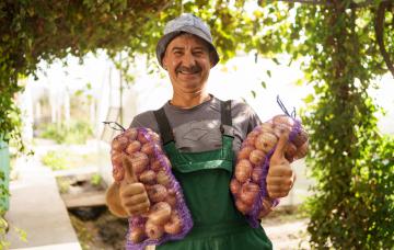 Llevar patatas podría ser una buena medida de la salud de los mayores Hombre mayor sonriendo cargando dos bolsas de patatas