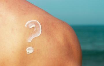 Protector solar: dudas de cuándo usarlo Interrogante hecho con protector solar en la espalda de un hombre en la playa