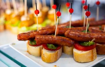Chistorra dispuesta en pinchos con pan y tomate sobre una bandeja