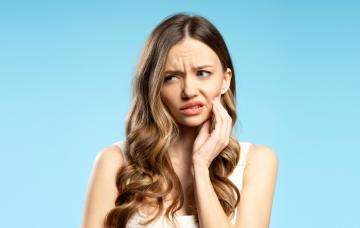 Dolor de muelas por caries tras despertar una lesión inactiva Mujer con pelo largo se lleva la mano a la mandíbula por dolor de muelas