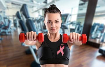 Levantar peso tras un cáncer de mama Mujer en el gimnasio levanta pesas con un lazo en apoyo al cáncer de mama