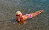 Una mujer mayor sonríe a la cámara tumbada a la orilla del mar