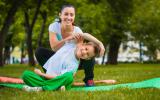 Un niño practica yoga en un parque con la ayuda de su profesora
