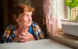 Mujer mayor mira por la ventana con gesto triste