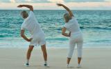Una pareja de adultos mayores hace gimnasia en la playa al atardecer