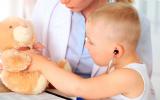 Un niño pequeño ausculta a su osito de peluche en presencia de su doctora