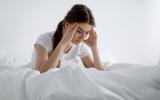 Mujer joven se incorpora en la cama con gesto de dolor