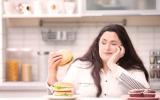 Una chica joven con sobrepeso mira una hamburguesa que tiene en la mano