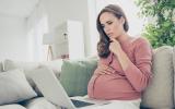 Mujer embarazada observa preocupada información en la pantalla de un portátil