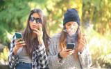 Dos chicas adolescentes fuman en un parque mientras consultan sus smartphones