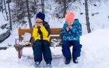 Dos niños comen en un banco rodeados de nieve
