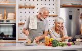 Pareja de adultos mayores cocinan alimentos saludables consultando una tablet