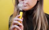 Chica rubia vapeando con su cigarrillo electrónico amarillo